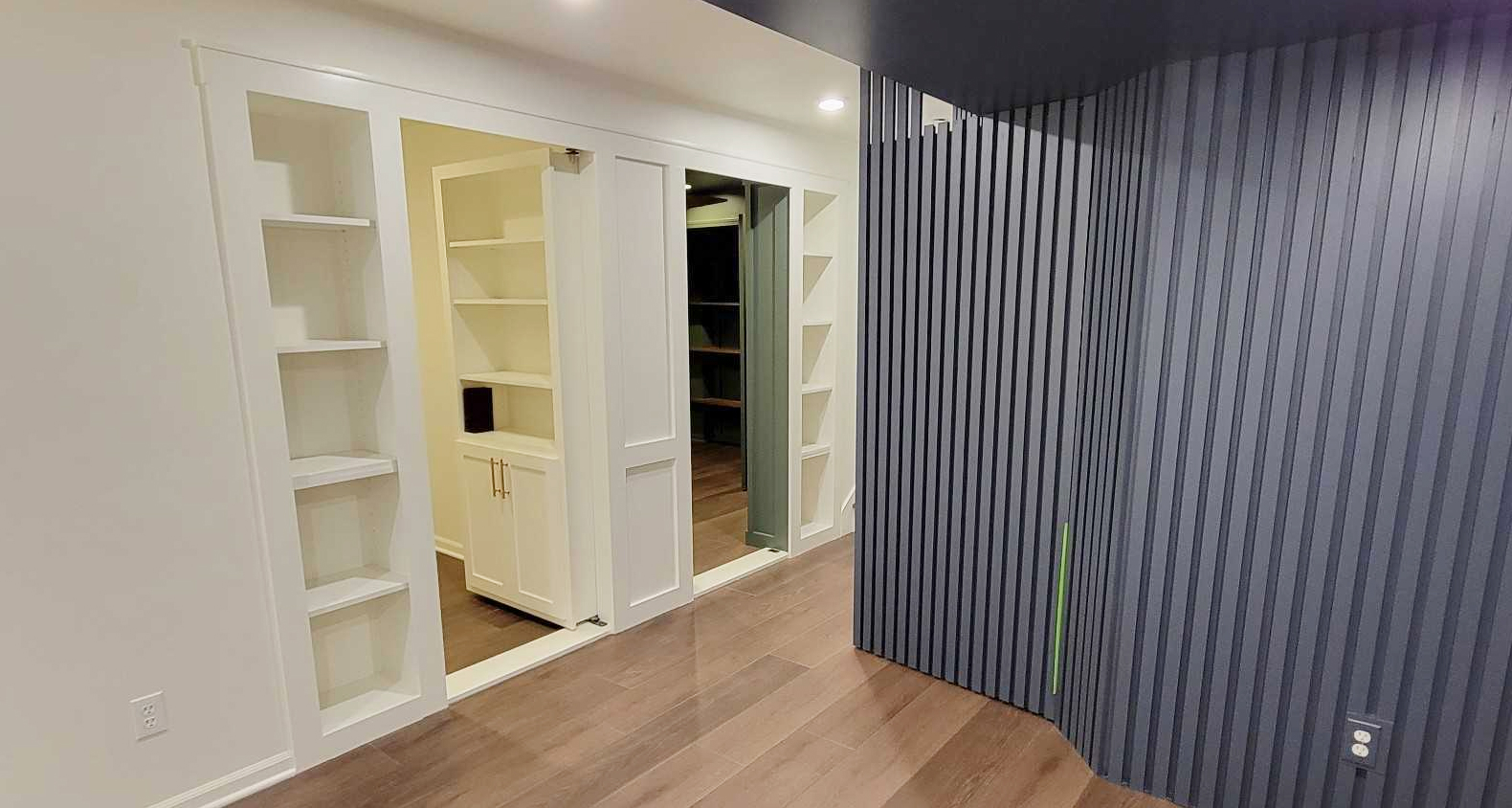 Two Murphy doors disguised as bookshelves open into an office and a bathroom. There is a navy blue slat accent wall on the right.